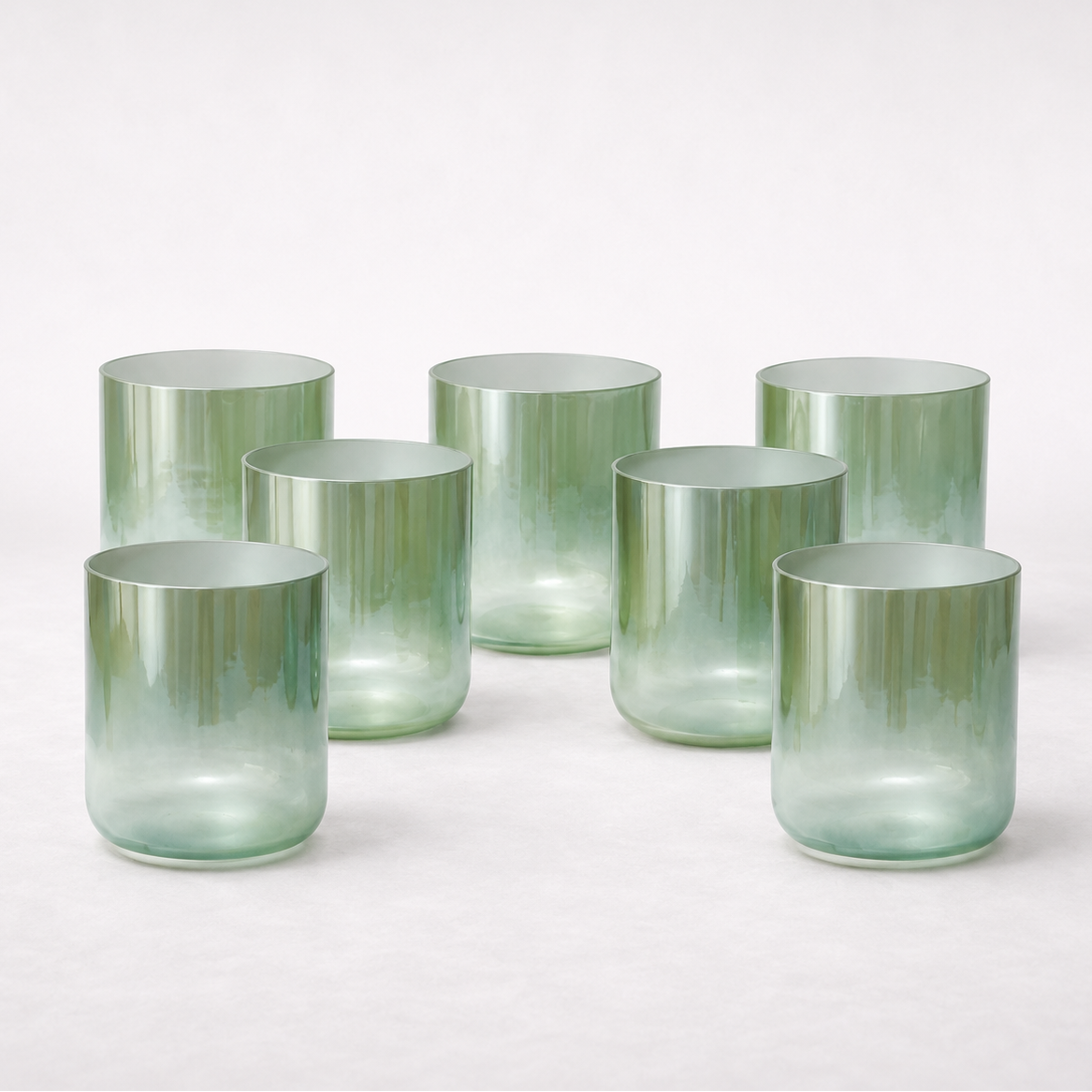 Seven translucent sage-green crystal singing bowls arranged in a harmonious formation on a soft neutral background, featuring Terratone’s signature earth-inspired gradient finish and minimalist aesthetic.